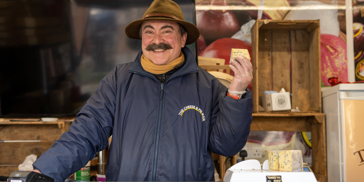 Cheese seller pictured holding cheeses at his stall