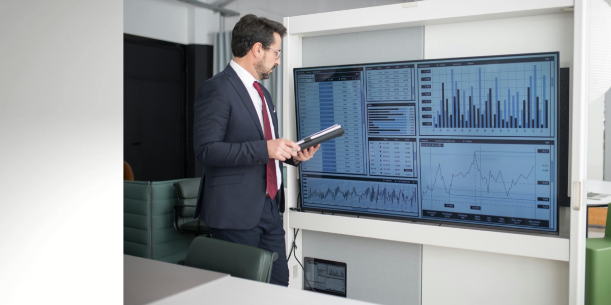 Man stands at smart screen and looks at business related graphs