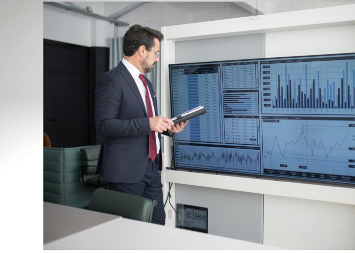 Man stands at smart screen and looks at business related graphs